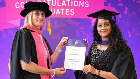 Two people in graduation attire; one hands a certificate to the other